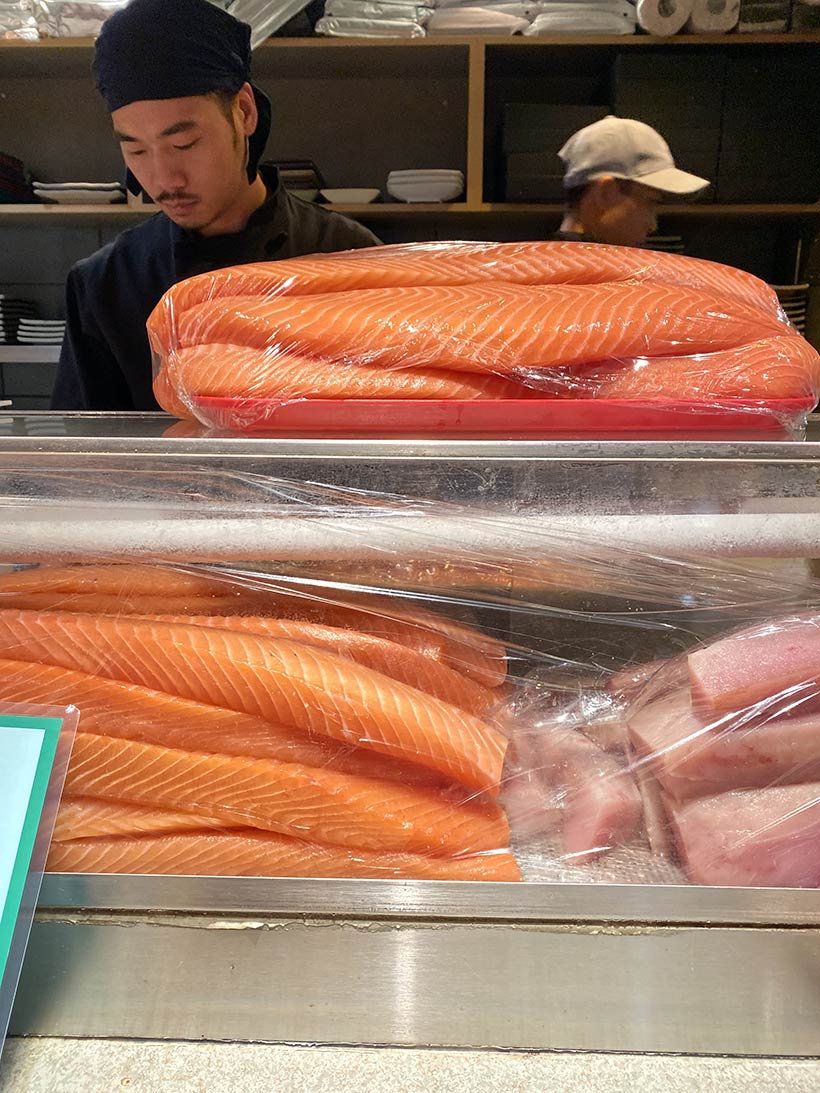 Sushiman trabalha em frente a várias tiras de salmão